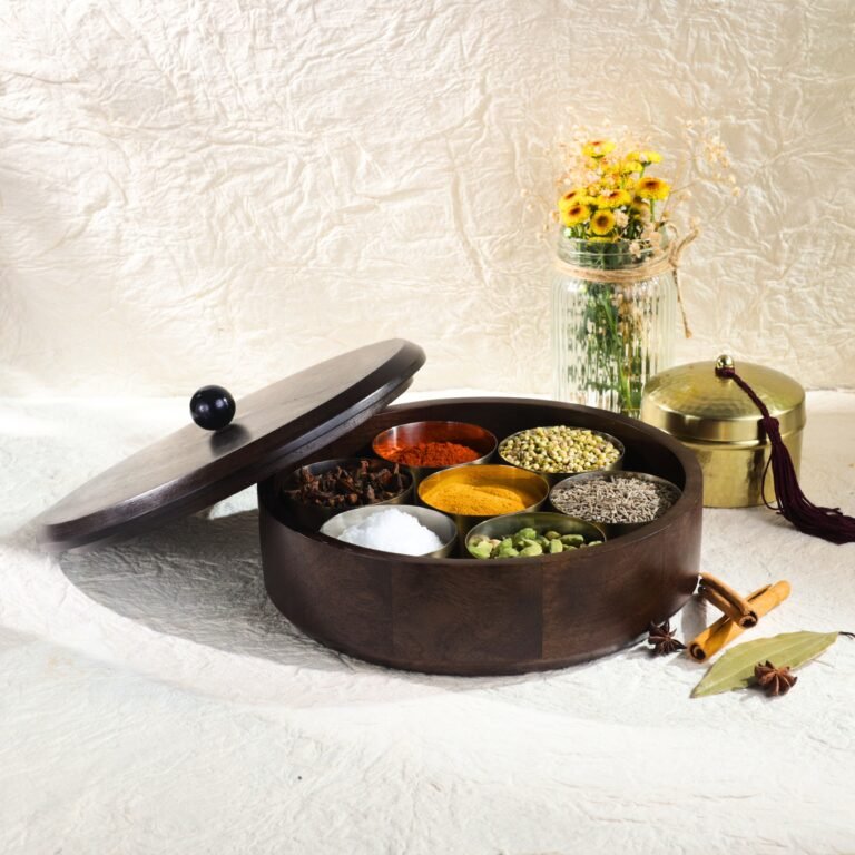 "- Premium Wooden Spice Box – Handcrafted from seasoned wood, offering durability, rich natural grain, and a polished finish - Carved Lid with Painted Accents – Intricate hand-carving with contrast detailing adds a modern yet timeless artisanal touch - Includes Metal Containers – Comes with round open metal spice containers for easy masala storage, herbs, dry fruits, or tea leaves - Freshness Locking Wooden Lid – Snug-fit lid with a sleek knob ensures flavors and aromas stay preserved longer - Multi-Purpose Storage – Use as a masala box, spice organizer, dry fruit box, or tea storage for an organized kitchen