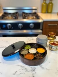 "- Premium Wooden Spice Box – Handcrafted from seasoned wood, offering durability, rich natural grain, and a polished finish - Carved Lid with Painted Accents – Intricate hand-carving with contrast detailing adds a modern yet timeless artisanal touch - Includes Metal Containers – Comes with round open metal spice containers for easy masala storage, herbs, dry fruits, or tea leaves - Freshness Locking Wooden Lid – Snug-fit lid with a sleek knob ensures flavors and aromas stay preserved longer - Multi-Purpose Storage – Use as a masala box, spice organizer, dry fruit box, or tea storage for an organized kitchen