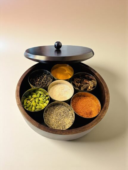 "- Premium Wooden Spice Box – Handcrafted from seasoned wood, offering durability, rich natural grain, and a polished finish - Carved Lid with Painted Accents – Intricate hand-carving with contrast detailing adds a modern yet timeless artisanal touch - Includes Metal Containers – Comes with round open metal spice containers for easy masala storage, herbs, dry fruits, or tea leaves - Freshness Locking Wooden Lid – Snug-fit lid with a sleek knob ensures flavors and aromas stay preserved longer - Multi-Purpose Storage – Use as a masala box, spice organizer, dry fruit box, or tea storage for an organized kitchen